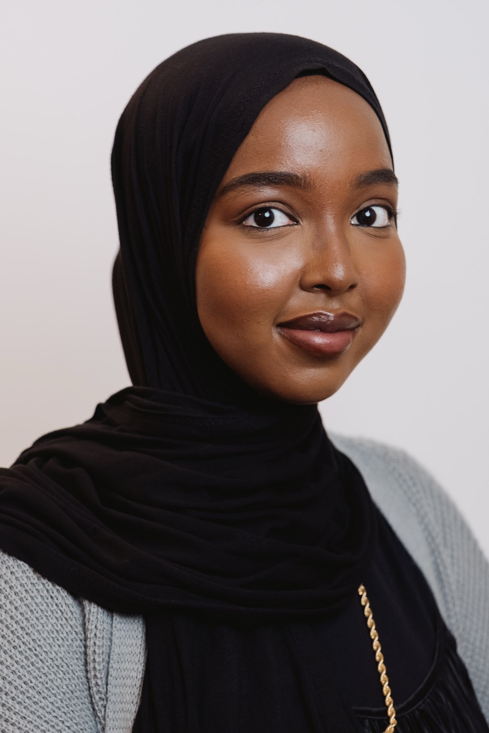 Professional headshot of a young woman wearing a black hijab, soft studio light
